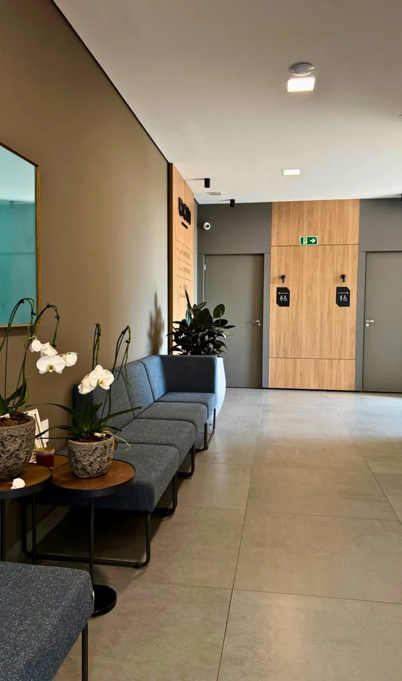 Hall de espera com sofá, orquídeas e a sinalização DON ao fundo