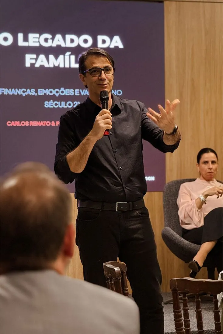 Palestrante ao microfone diante do telão O Legado da Família