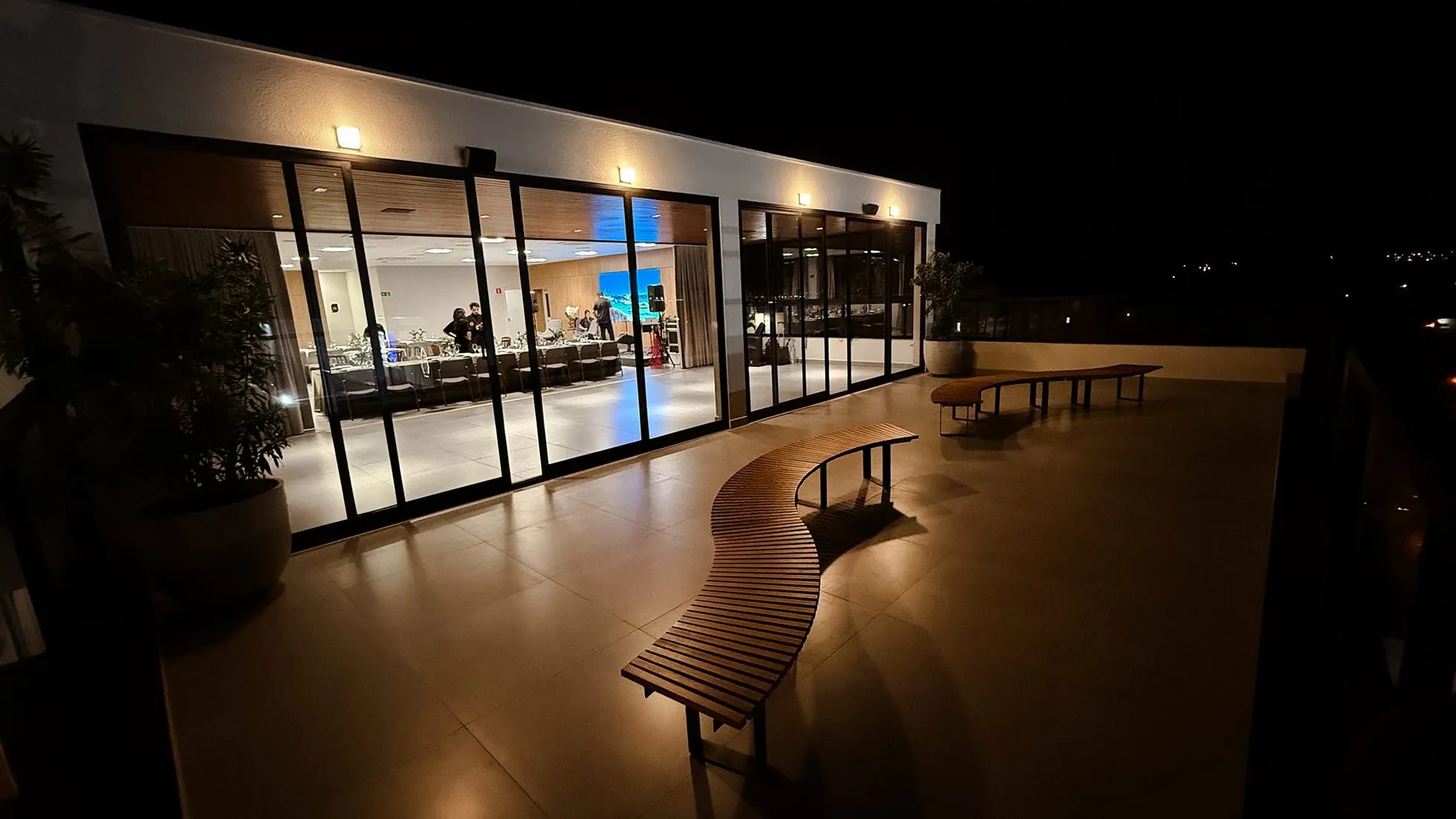 Vista noturna do rooftop com bancos e a avenida ao fundo